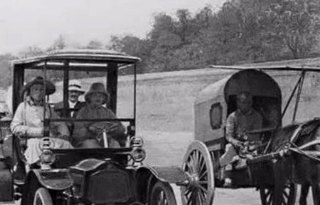 An image showing cars and horse-drawn carriages running parallel on the road