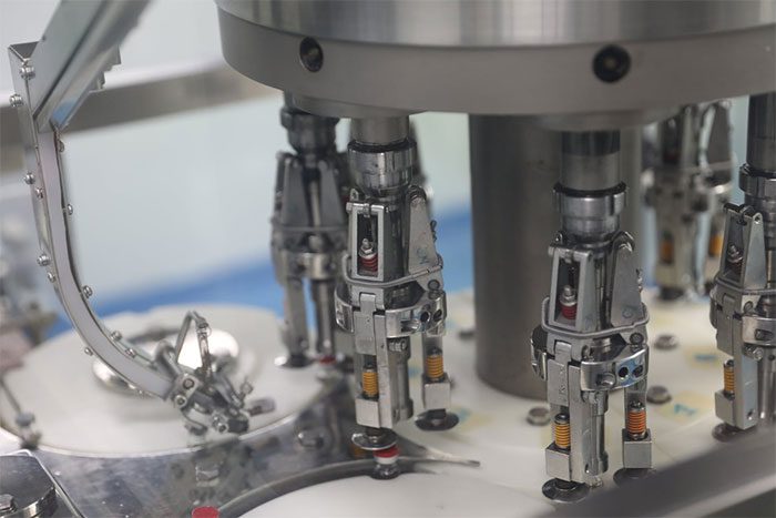The vaccine vials move along the conveyor to the aluminum cap sealing machine.