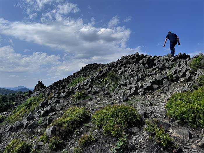 Czech locals climb to the top of the Panská skála basalt rock and admire the distant scenery.