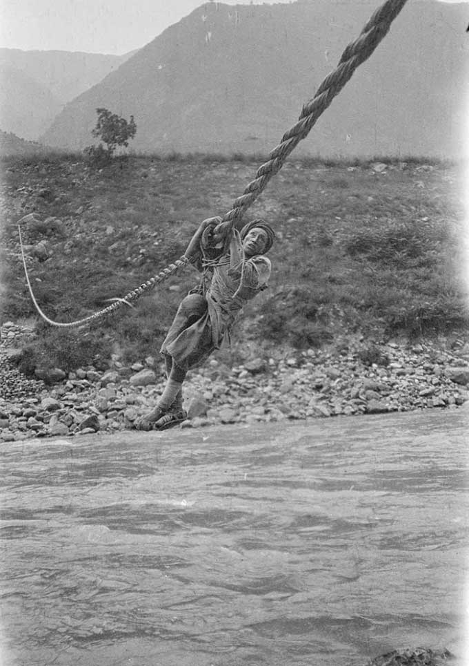 A man holding onto a rope to cross the river, photographed in Sichuan.