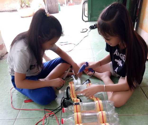 Two children creating life jackets from plastic bottles.