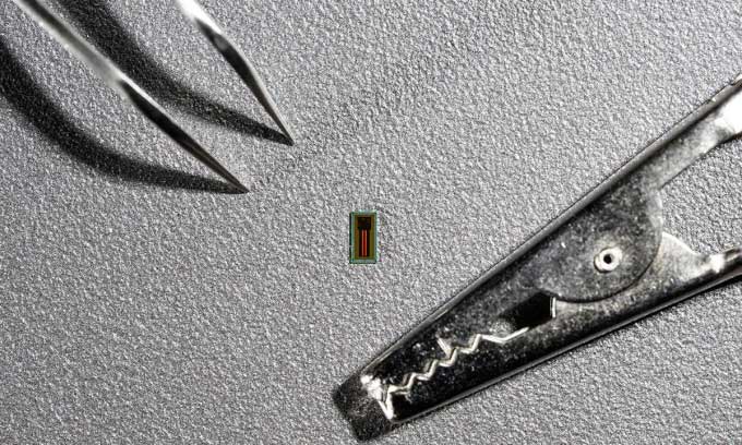 The super-small MiBMI chip next to a pair of tweezers and a crocodile clip.