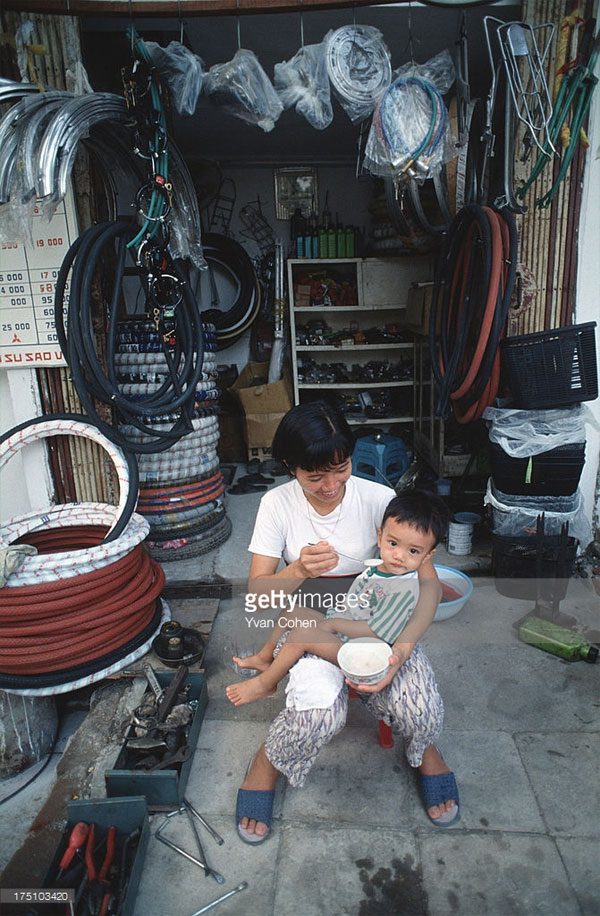 A woman feeding her child outside a bicycle parts shop.