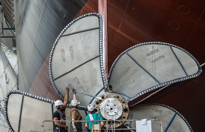 Workers are tightening bolts on one of the propellers of the USS Gerald R. Ford using a torque wrench.