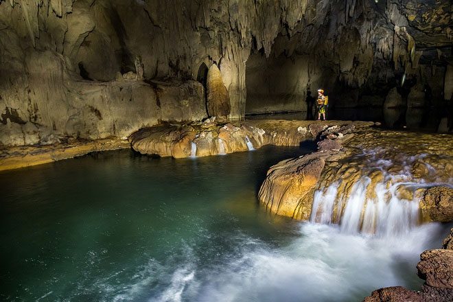 Tourists kayaking or wading through the waterfalls inside the caves