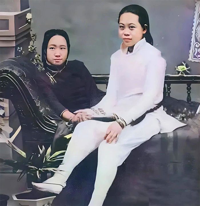 Two courtesans posing for a photo on a chair.