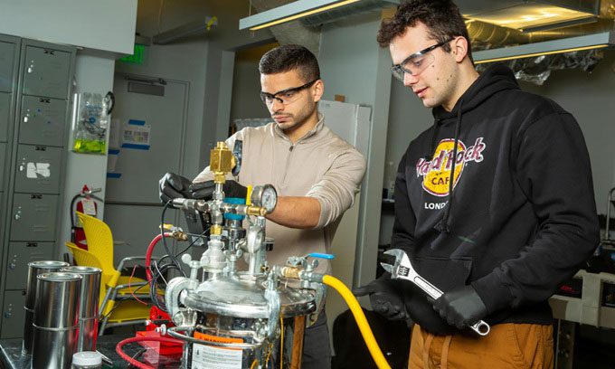 Two MIT researchers Aly Kombargi (left) and Niko Tsakiris (right) with the new hydrogen reactor.