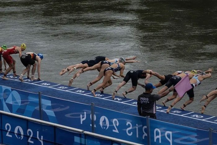 Triathlon athletes swimming through the Seine River at the Paris Olympics.