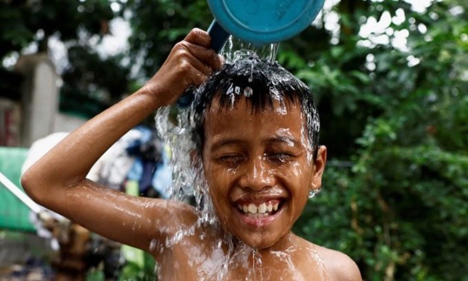 A boy pours water over his head to cool off in a densely populated area of Jakarta on May 16, 2024.