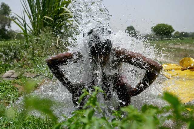 A man bathing under a water pipe during the heatwave