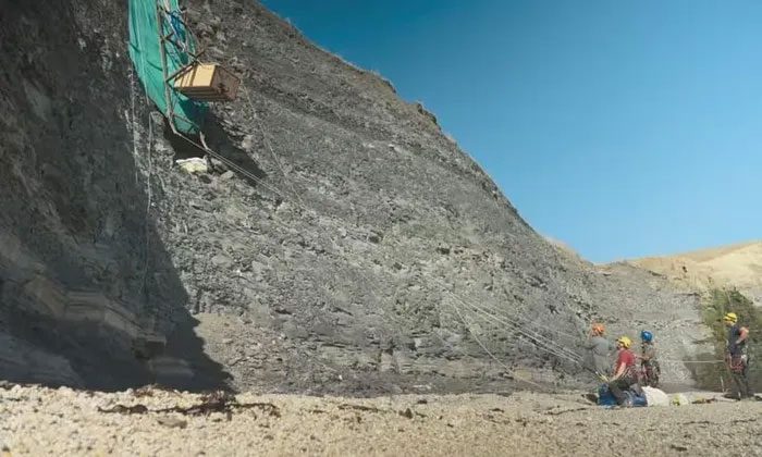 Biologists rappel down to excavate fossils on the steep cliff.