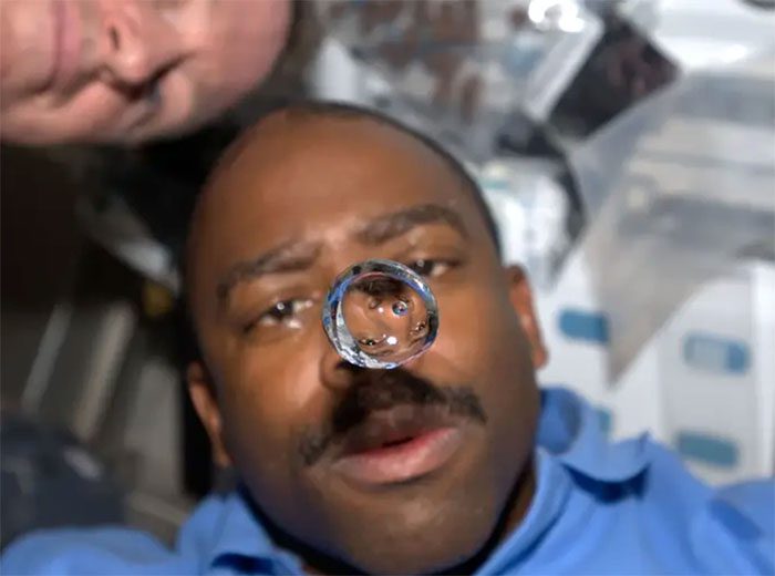 Astronaut Leland Melvin observing a floating water droplet in the shuttle cockpit