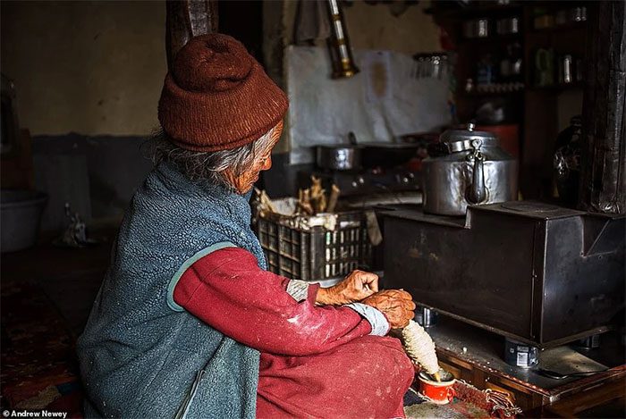 An elderly man spinning wool by the fire at home in Purne