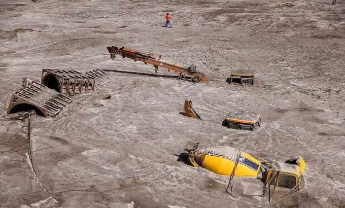 A man walks past construction vehicles engulfed in debris