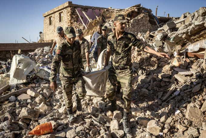 Moroccan Royal Armed Forces carry a body from a destroyed house.