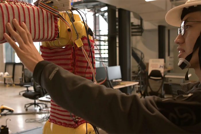 The garment wraps around the robot's arm and is connected to a power source.
