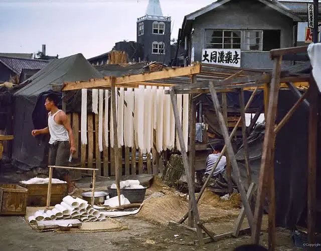 A street artisan making noodles with simple drying racks and straw below