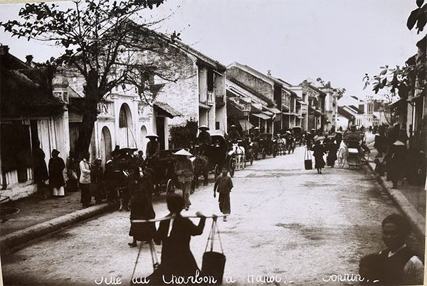Hàng Than Street in 1951 with many horse-drawn carriages, cycle rickshaws, and bustling women carrying goods.