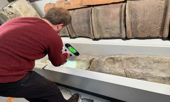 Researcher 3D scanning plaster-covered remains in a coffin.