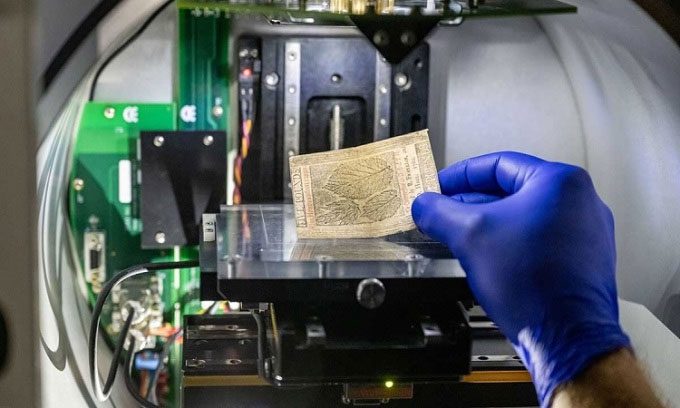 A researcher examines a bill under a spectroscopic device.