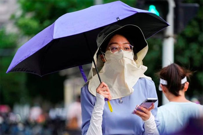 A woman shields herself from the sun with a hat, mask, and umbrella in China.