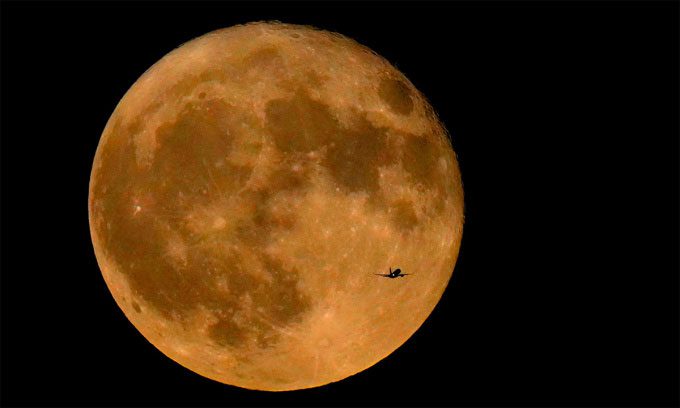 An airplane flying northwest over Lake Michigan, with the Supermoon in the background on July 3, 2023.