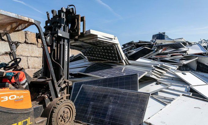 Forklift dropping solar panels into a large pile.