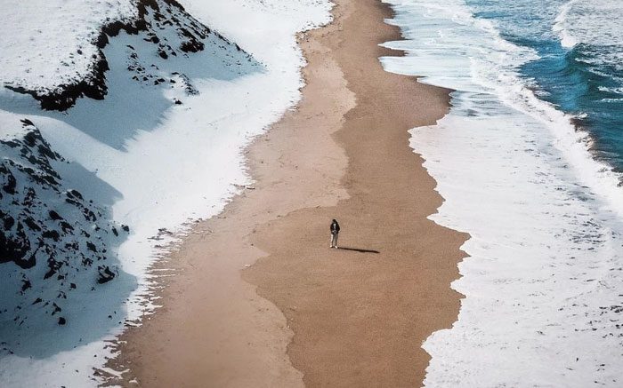 An image of a beach, with snow on one side, the sea on the other, and a stretch of golden sand in the middle.