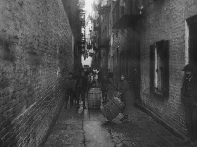 Children playing with barrels in an alley between apartment buildings