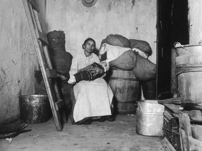 An Italian immigrant sitting with a child in a small, rundown apartment