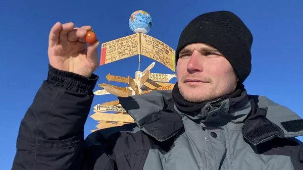A scientist at the Vostok Research Station next to a tomato grown in Antarctica