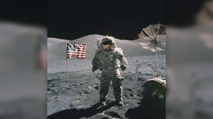 An astronaut from Apollo 17 walking on the Moon's surface, with the American flag in the background.