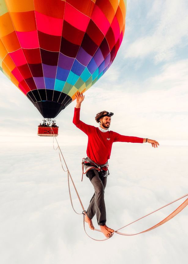 A man walking a tightrope between two hot air balloons.