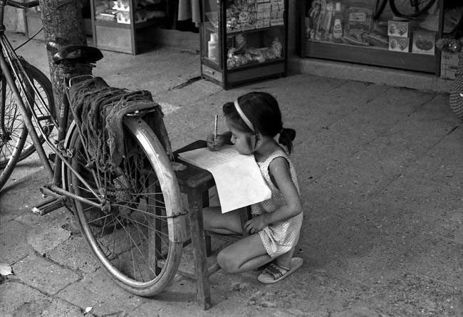 A girl practicing writing on the sidewalk of the old quarter.