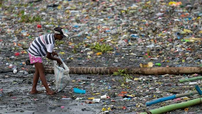 A woman collecting plastic cups along the trash-filled banks of the Pasig River in Manila