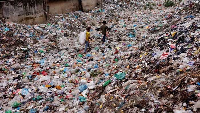 Two children walking through a garbage-filled area to collect plastic materials in Bangladesh, January 24