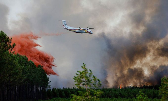 Firefighting aircraft dropping fire retardant to extinguish flames in Guillos