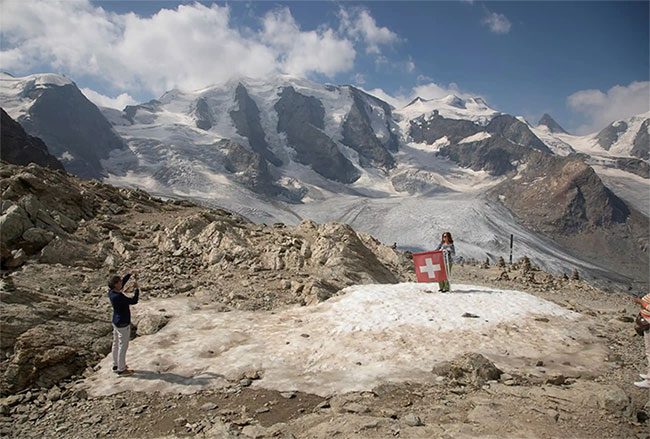 A woman taking a photo with the Swiss flag near the peak of Piz Palü.