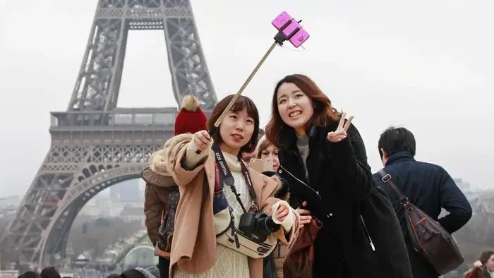 Two Japanese tourists take a photo in front of the Eiffel Tower in Paris.