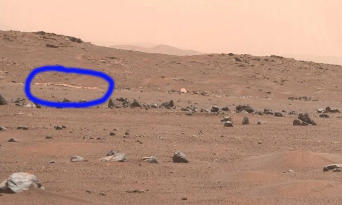 The parachute (the thin yellow line in the upper left corner of the frame) of Perseverance in a distant shot.