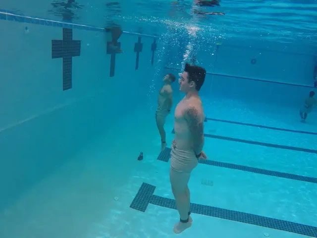 A student performing an underwater swim while bound by hands and feet.