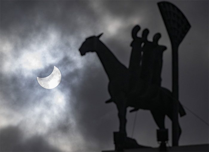 The Moon partially obscures the Sun behind the "Horseman of the Apocalypse" statue