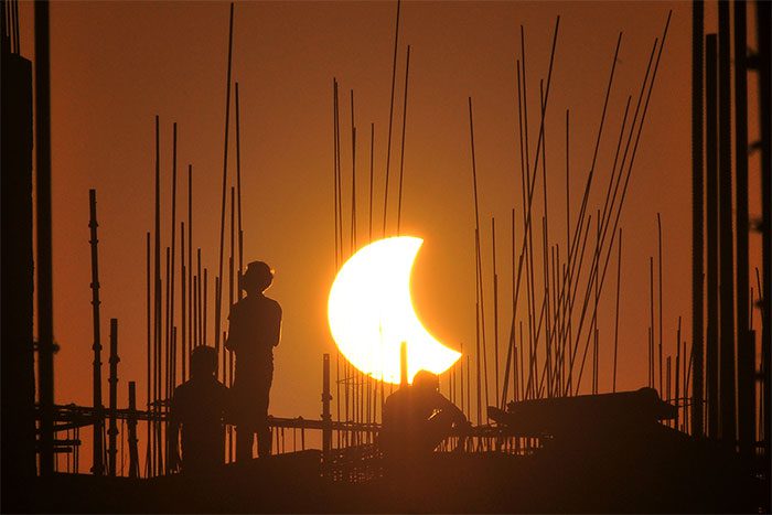 The shadows of workers stand out in front of the partial solar eclipse.