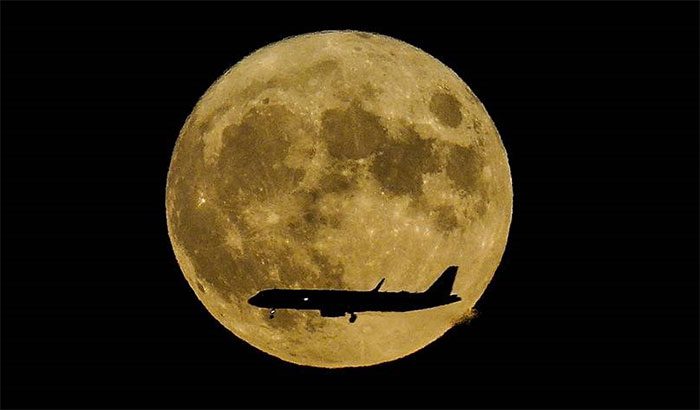 The supermoon rises as a jet approaches John F. Kennedy International Airport.