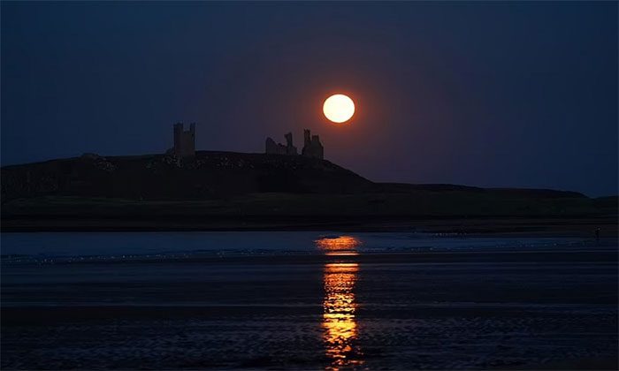 The moon rises behind Dunstanburgh Castle in Northumberland, England.
