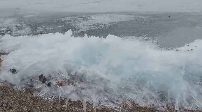 Waves crashing against the shore while the water surface remains frozen.