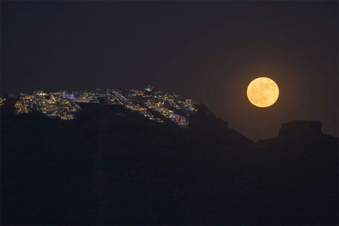 "Strawberry Moon" rising behind the village of Imerovigli on the caldera of Santorini