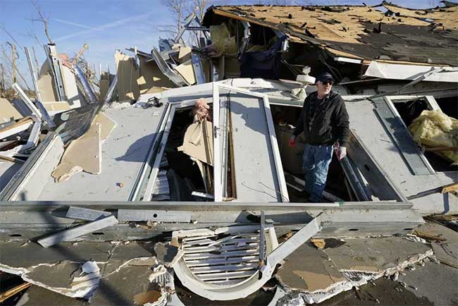 A man in Mayfield stands next to a destroyed house.