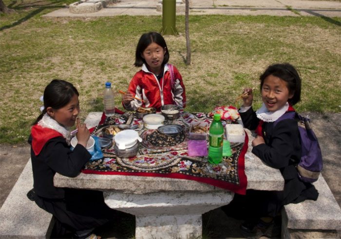 Three female students enjoying an outdoor meal at a park in Pyongyang.